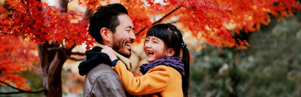 Dad and daughter smiling with fall trees in background