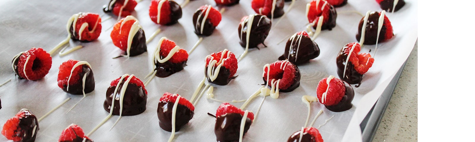 Rows of chocolate-dipped raspberries with a white chocolate drizzle on parchment paper