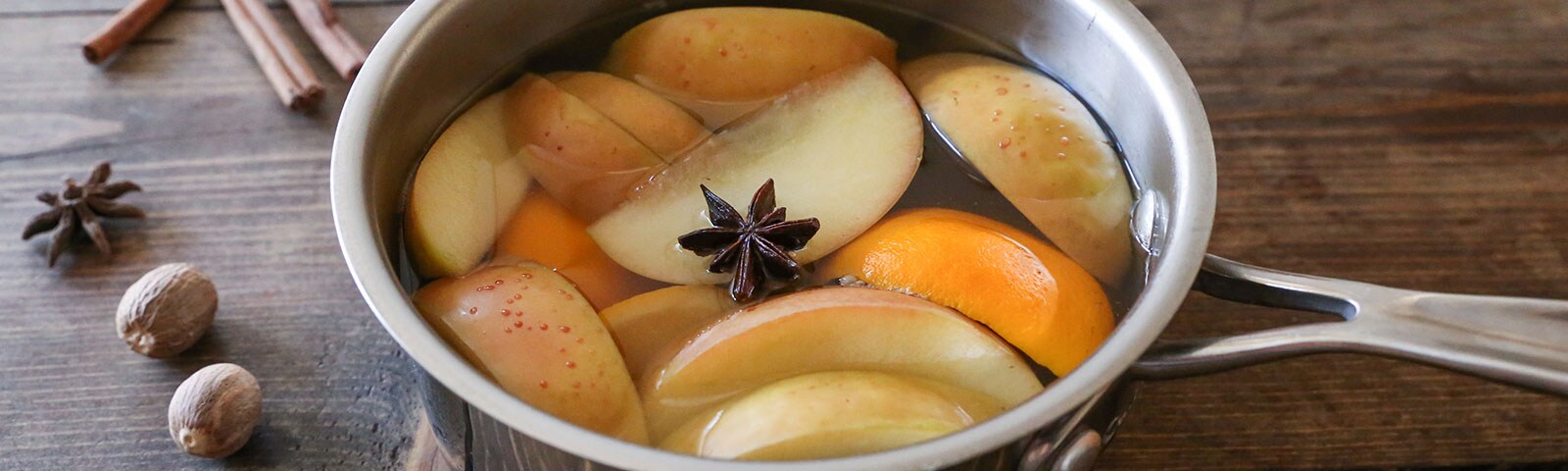 A metal pot filled with water, orange and apple slices, and one star anise on a counter A metal pot filled with water, orange and apple slices, and one star anise on a counter