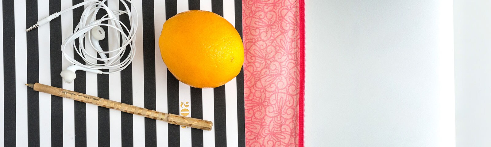 Lemon on top of black and white stripe tablecloth with ears buds and pen