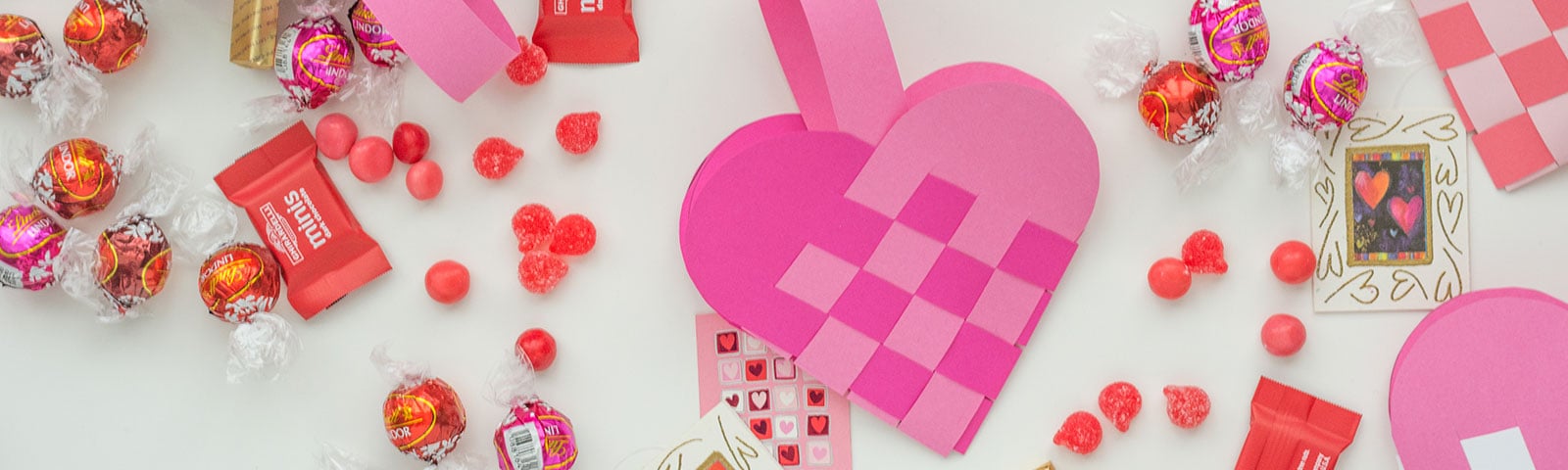 Finished handmade woven heart treat bags in pink cardstock paper surrounded by candy