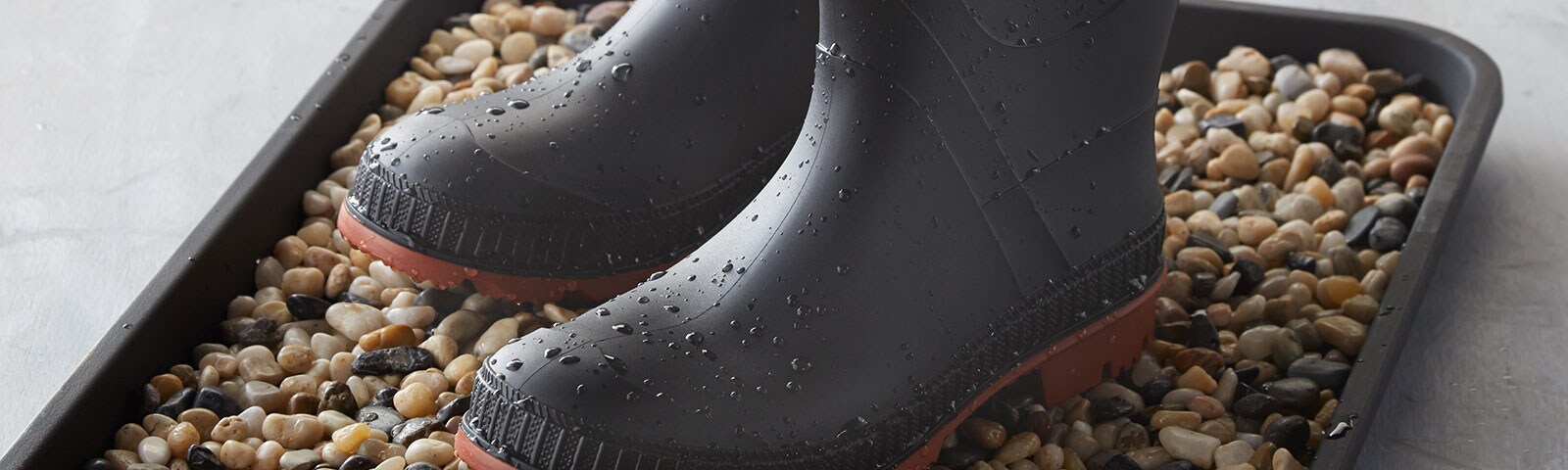 Wet rain boots atop a bed of pebbles sitting in a tray Wet rain boots atop a bed of pebbles sitting in a tray