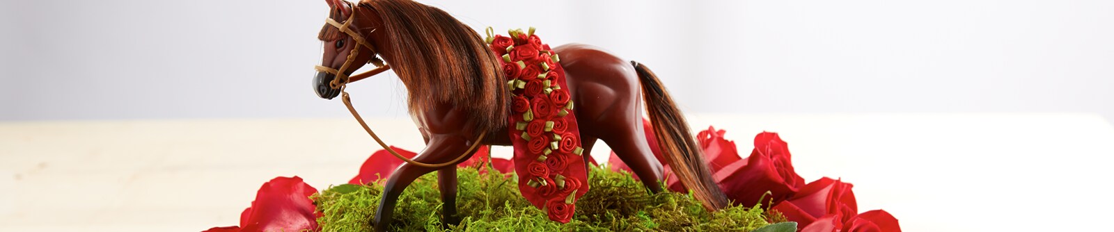 Close crop of a small horse figurine with a sash of roses on a field of fake grass
