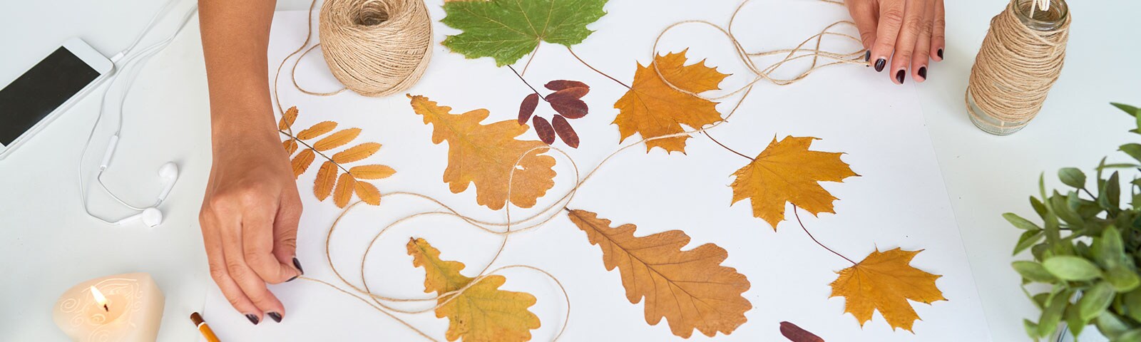 White table scattered with fall leaves, a candle, a mobile phone and twine with two hands grabbing it from each end White table scattered with fall leaves, a candle, a mobile phone and twine with two hands grabbing it from each end