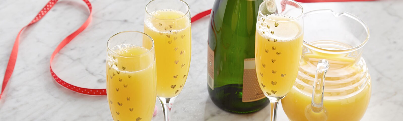 Crafty champagne flutes filled with mimosas in the foreground and candy hearts scattered on a marble countertop Crafty champagne flutes filled with mimosas in the foreground and candy hearts scattered on a marble countertop