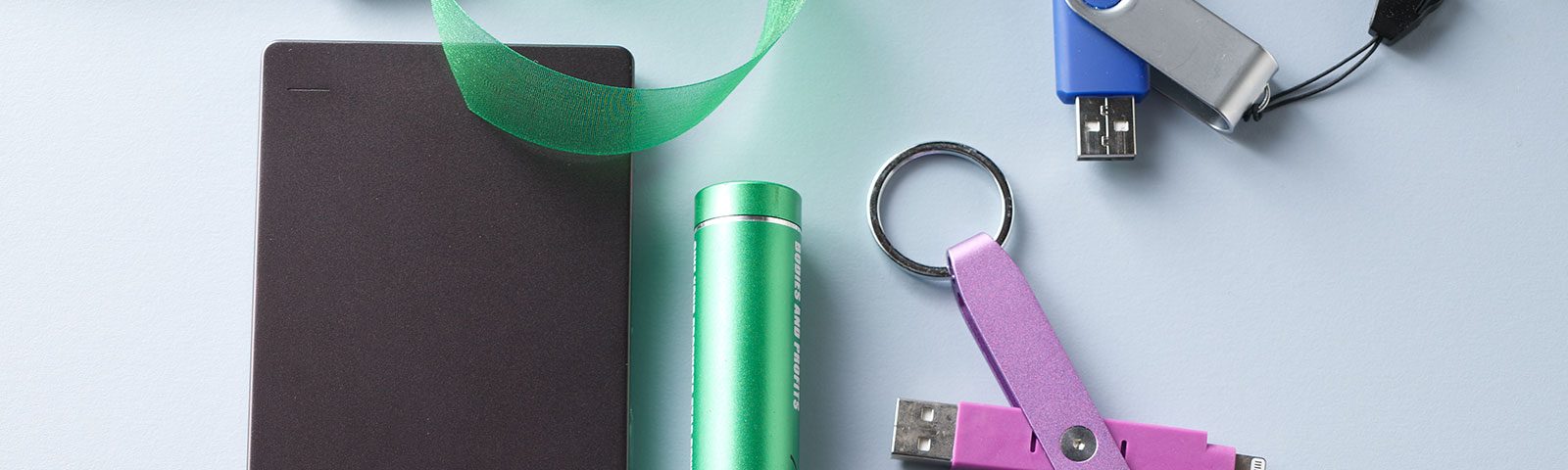 White table top with a flash drive, external hard drive, earbud headphones, spiral notebook and USB cord scattered about White table top with a flash drive, external hard drive, earbud headphones, spiral notebook and USB cord scattered about