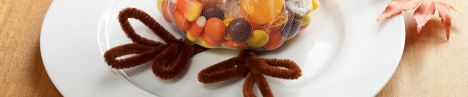 A bag of mixed candy with turkey legs made from brown pipe cleaners sit on a white plate A bag of mixed candy with turkey legs made from brown pipe cleaners sit on a white plate