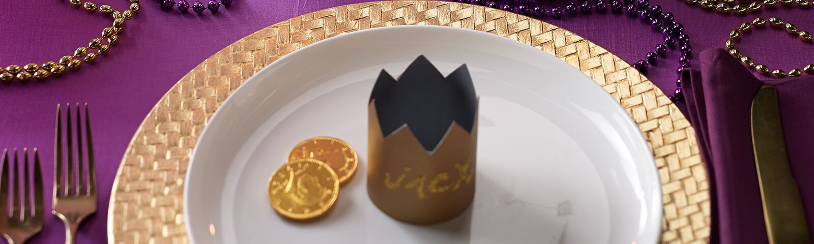 Mardi Gras-themed table decor featuring gold chargers and placemats on a purple tablecloth surrounded by gold and purple beads Mardi Gras-themed table decor featuring gold chargers and placemats on a purple tablecloth surrounded by gold and purple beads
