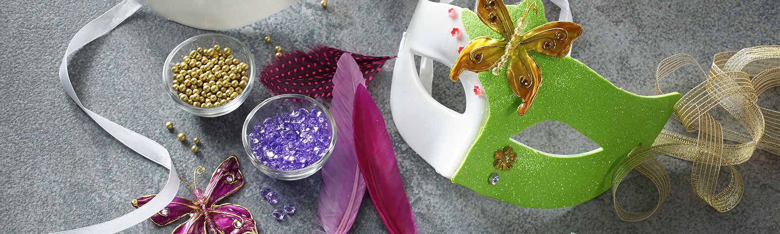 Two decorated Mardi Gras masks next to bowls of beads and ribbon strewn about Two decorated Mardi Gras masks next to bowls of beads and ribbon strewn about