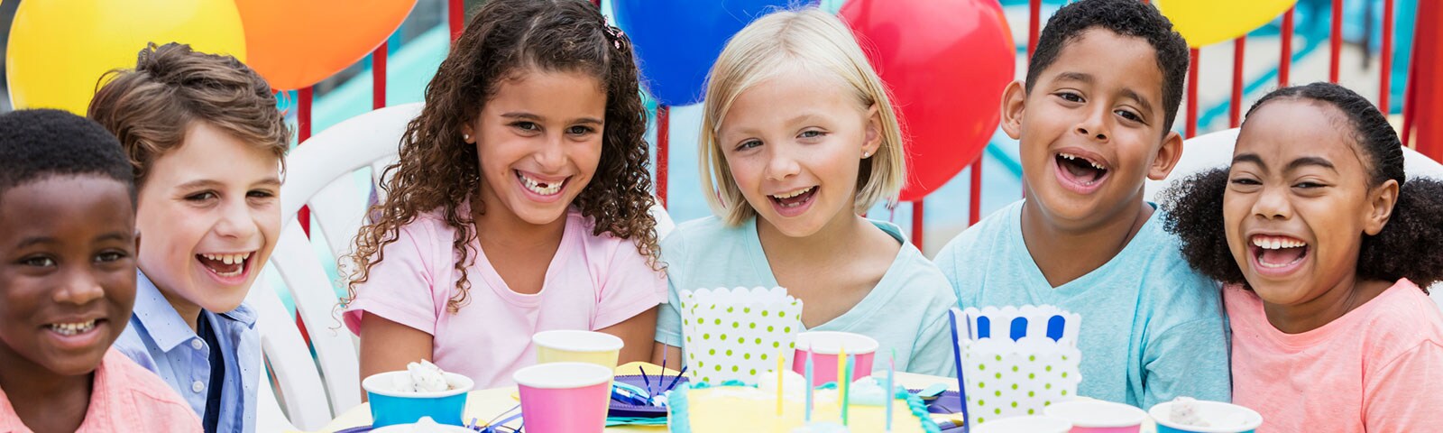 Six kids laughing while sitting around a table with a birthday cake in the middle Six kids laughing while sitting around a table with a birthday cake in the middle