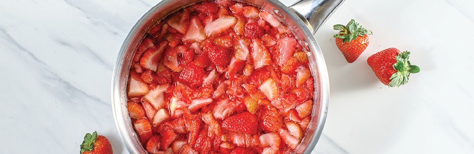 saucepan with boiled water and sugar with strawberries simmering